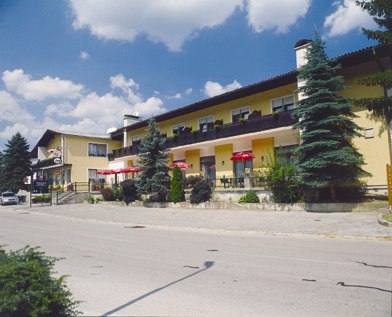 Café Restaurant Bernhart, © z.V.g. von Café Restaurant Bernhart, Foto Jürgen Bernhart Gelbes Gebäude mit Café und Restaurant, umgeben von Bäumen, unter blauem Himmel.
