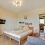 Bedroom, © Wachahof A cozy bedroom with a wooden floor, a double bed with yellow bed linen, a flat-screen TV on the wall and an open passageway to the kitchen.