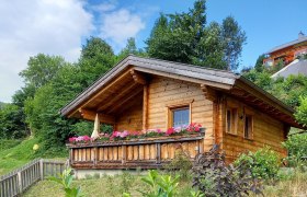Das Paradieschen, © Fam. Auer Holzhütte mit Blumen auf der Veranda in einer grünen Umgebung.