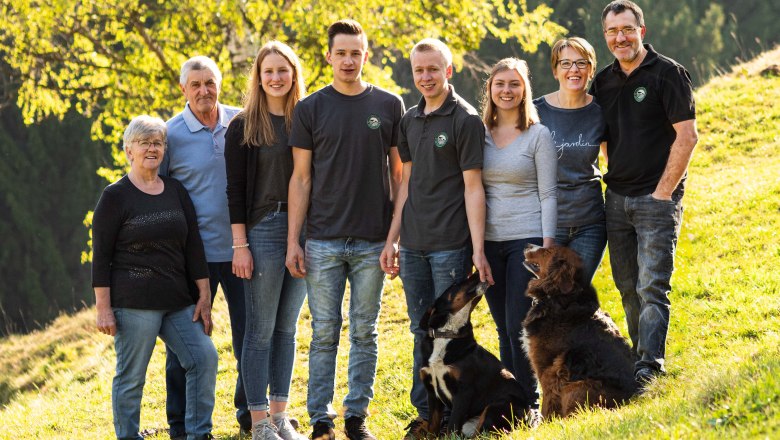 Kleinrath family, © Anni Putz A large family with two dogs is standing on a green meadow in front of a tree.
