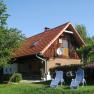 Wachahof Schwarz family, © Wachahof A rustic house with a red roof, surrounded by trees and garden furniture on a meadow.