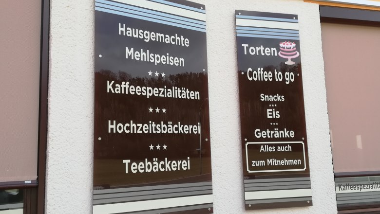 Coffee house Siaß' Eck, © Wiener Alpen Two brown signs on the wall with coffee house offers such as pastries and ice cream.