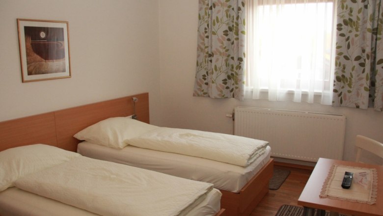 Ein Gästezimmer mit zwei Einzelbetten, einem Fenster mit Vorhängen, einem Tisch mit Fernbedienung und einem Bild an der Wand.