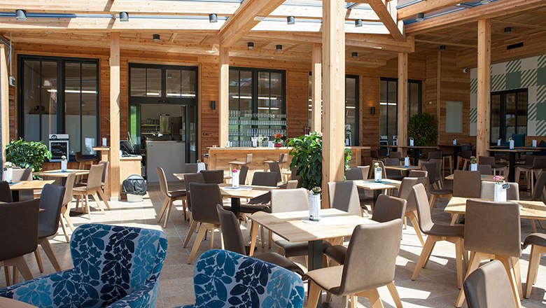 Ein modernes Kaffeehaus mit vielen Holzelementen, eckigen Tischen und braunen und blauen St&uuml;hlen.