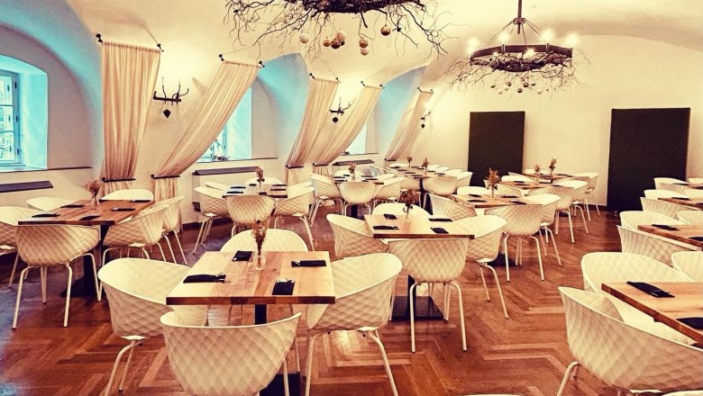 Eleganter Speisesaal mit Parkettboden, wei&szlig;en St&uuml;hlen, Holztischen und dekorativen Kronleuchtern.