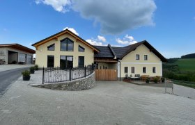 Gelbes Haus mit großen Fenstern auf gepflasterter Fläche unter blauen Himmel.