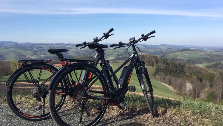 Two e-bikes are parked on a hill overlooking a hilly landscape.