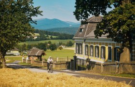 Eine Radfahrerin auf einer Landstra&szlig;e f&auml;hrt am Schloss Ziegersberg vorbei. Im Hintergrund der Wechsel.