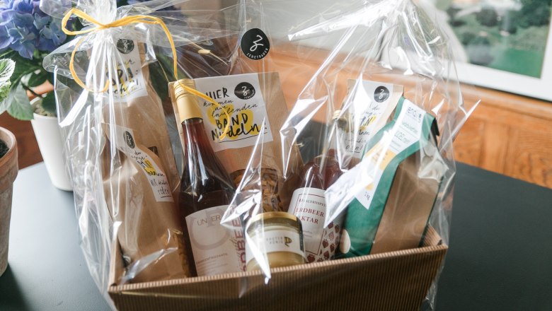 Geschenkkorb mit regionalen Produkten, verpackt in Folie, auf einem Tisch.