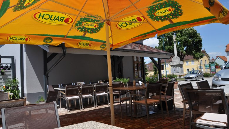 Outdoor area of a café with a yellow parasol and empty tables and chairs.