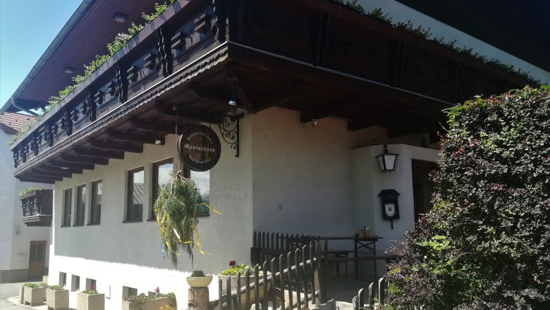 Traditionelles Gebäude mit Holzbalkon und Schild mit der Aufschrift "Mostschank".