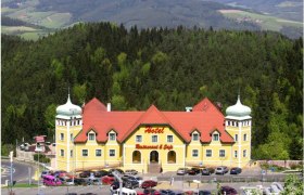 Yellow hotel with red roofs in a green, hilly landscape.
