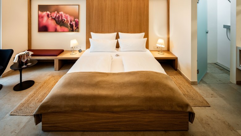 Modernly furnished hotel room with double bed, bedside tables, lamps and a picture on the wall.