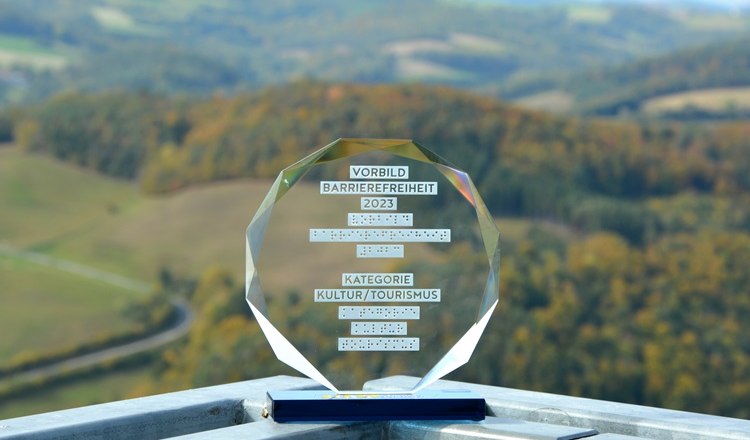 Eine Auszeichnung f&uuml;r Barrierefreiheit 2023 steht auf einem Gel&auml;nder mit Landschaft im Hintergrund. Die Aussichtsplattform ist mit einem Aufzug erreichbar.