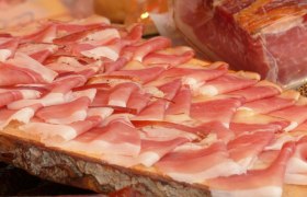 Nahaufnahme von d&uuml;nn geschnittenem Speck auf einem Holzbrett.