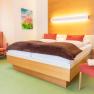 Ein gemütliches Doppelzimmer mit einem großen Bett, roten Kissen, einem Sessel, einem Stuhl und einem Gemälde an der Wand.