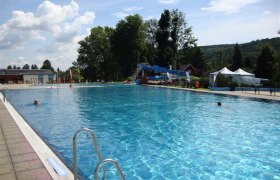 A large outdoor pool with clear water, surrounded by trees and hills under a blue sky.
