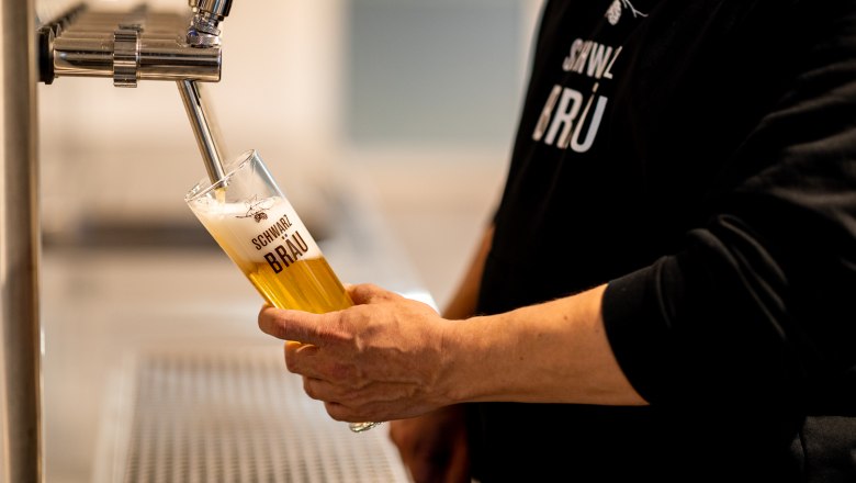 Eine Person zapft Bier in ein Glas mit der Aufschrift "Schwarzbr&auml;u".