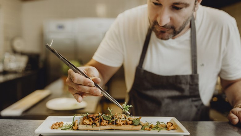 A chef arranges a dish on a plate with a pair of tweezers.