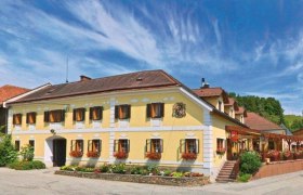 Traditionelles Gasthaus mit gelber Fassade, umgeben von grüner Landschaft und blauem Himmel.