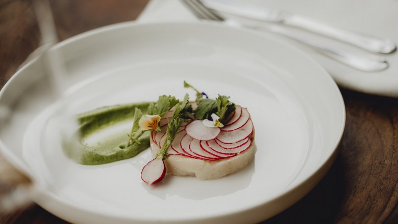 Ein Tellergericht mit Saibling, Radieschen und Wasabi-Creme, dekoriert mit essbaren Blüten.