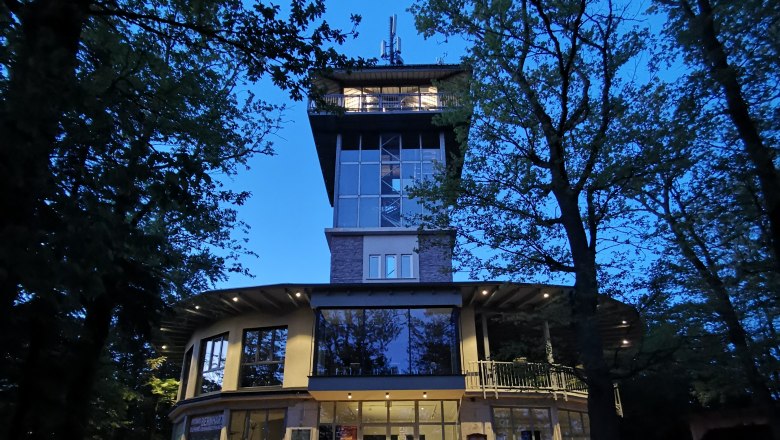 Ovales Gebäude mit Aussichtsturm aus Glas bei Nacht.