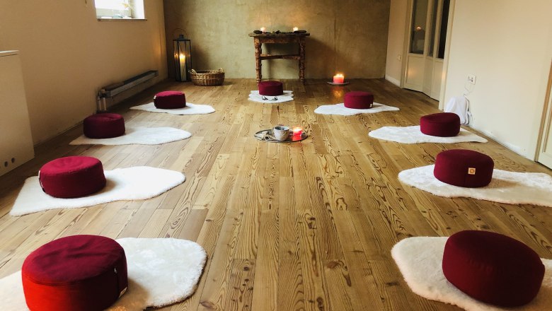 Meditation room with red cushions on white mats, candles and wooden floor.