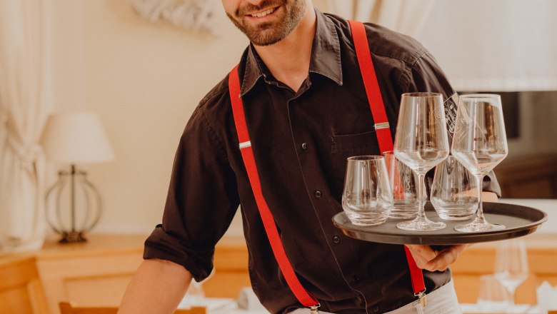 A waiter with red suspenders serves glasses in a restaurant.