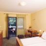 A cozy hotel room with double bed, desk, chest of drawers and balcony with a view of the greenery.