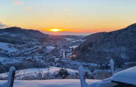 Winterlandschaft mit Sonnenaufgang über einem verschneiten Dorf in einem Tal.