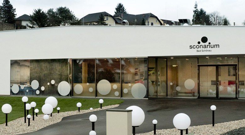 Modernes Gebäude mit Glasfront und dekorativen Kugeln vor dem Eingang.