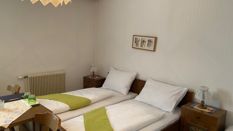 Gemütliches Doppelzimmer mit zwei Einzelbetten, Holzmöbeln und einer dekorativen Lampe.
