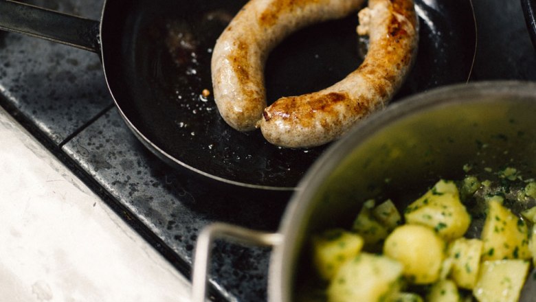 Bratwurst in Pfanne mit Kartoffeln im Topf.