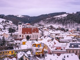 Kirchschlag t&eacute;li l&aacute;tk&eacute;pe h&oacute;f&ouml;dte h&aacute;ztetőkkel &eacute;s egy templommal az előt&eacute;rben.