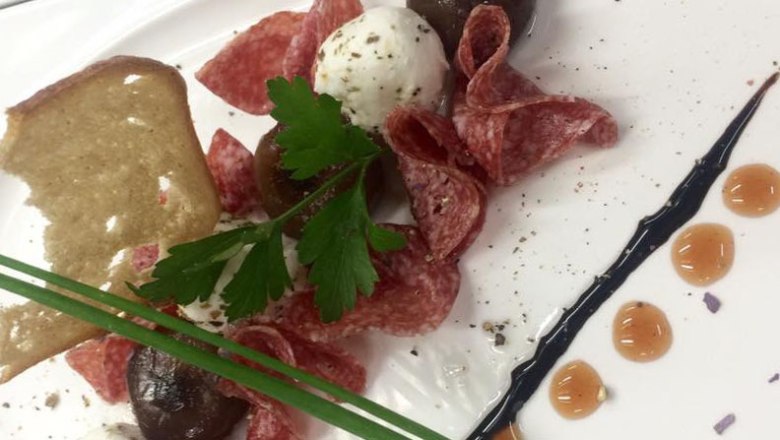 Ein Teller mit Salami, einem Ziegenkäsebällchen, Kräutern und einem Stück Brot.