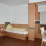 Ein einfach eingerichtetes Hotelzimmer mit Einzelbett, Schreibtisch und Holzverkleidung.