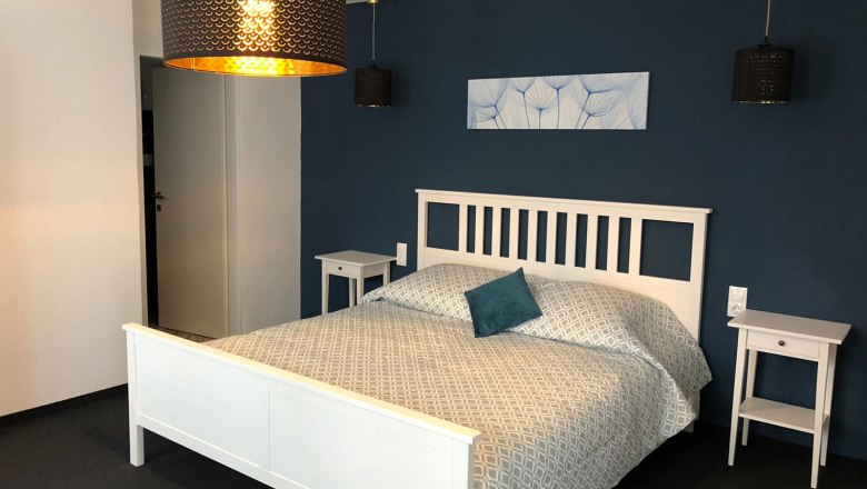 Modernes Doppelzimmer mit weißem Bett, blauer Wand und stilvollen Lampen.