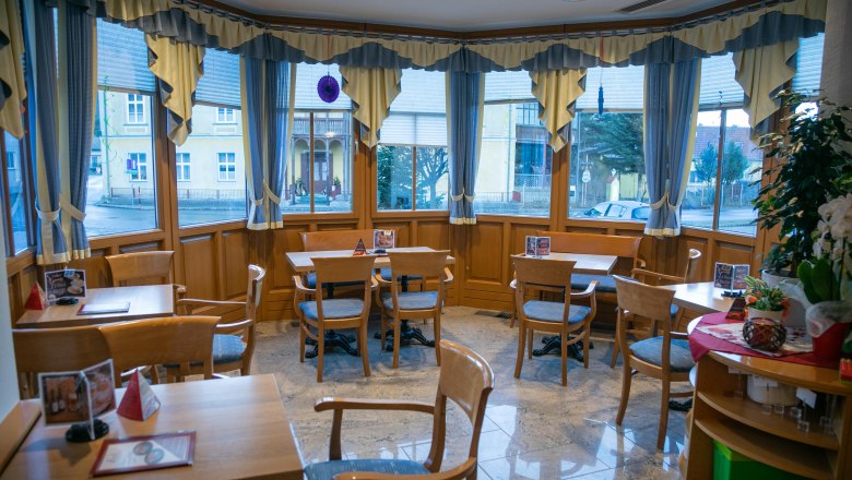 Innenansicht eines gemütlichen Cafés mit Holzmöbeln und großen Fenstern.