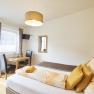 Bright guest room with bed, table, chairs and TV.