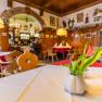 Gemütliches Gastzimmer mit Holzmöbeln, Tischdecken und Blumenvasen.