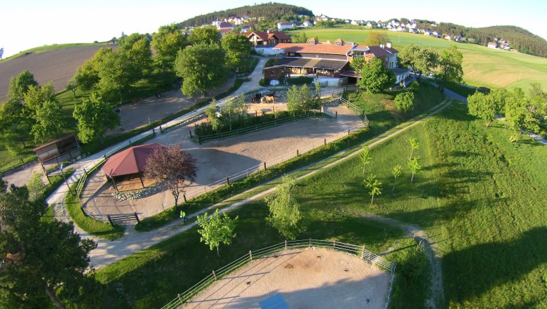 Aerial view of a rural estate with buildings, riding arenas and green landscape.