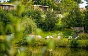 A peaceful garden with sun loungers by the pond, surrounded by trees and green vegetation.