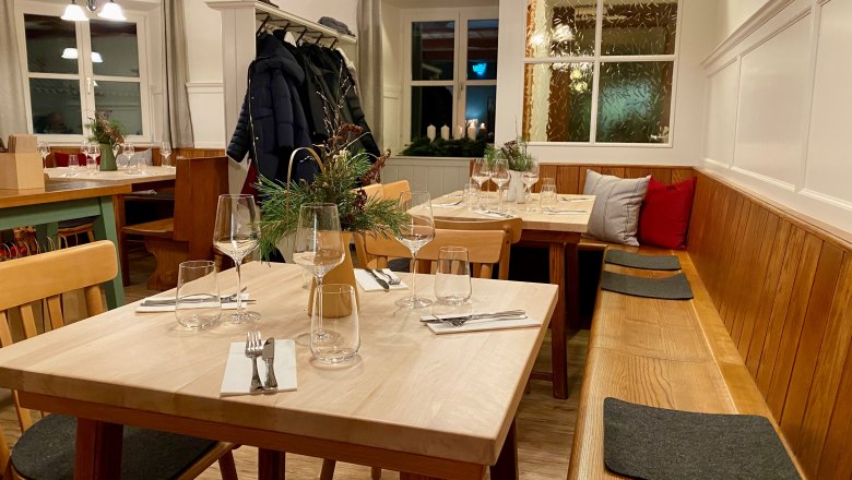 Die Gaststube mit Holzbank, Holztischen und Garderobe.