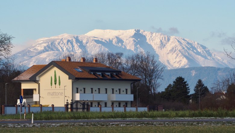 Geb&auml;ude mit der Aufschrift 'mattone apartments' vor schneebedecktem Berg im Hintergrund.
