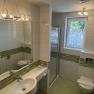 Modernes Badezimmer mit grünen Fliesen, Dusche, Waschbecken und WC.