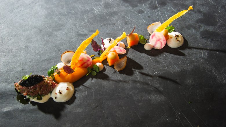 Künstlerisch angerichtetes Gourmetgericht auf dunklem Untergrund.