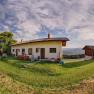 Panoramic view of a house on a meadow with trees and mountains in the background at sunset.