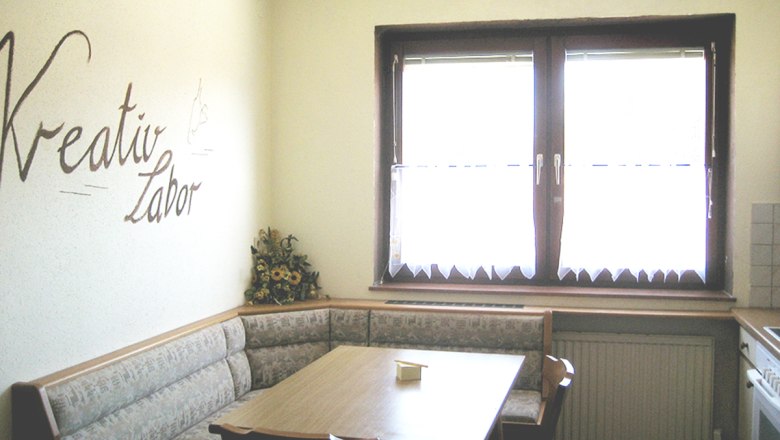 Kitchen with corner bench, table and 'Kreativ Labor' lettering on the wall.