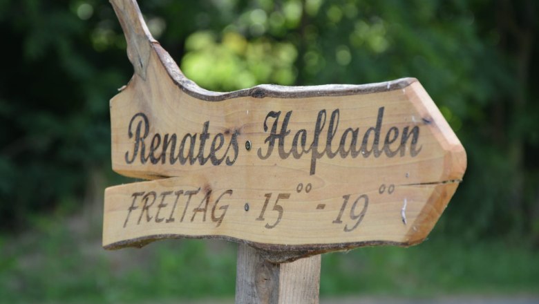 Holzschild mit der Aufschrift 'Renates Hofladen' und Öffnungszeiten 'Freitag 15-19 Uhr'.