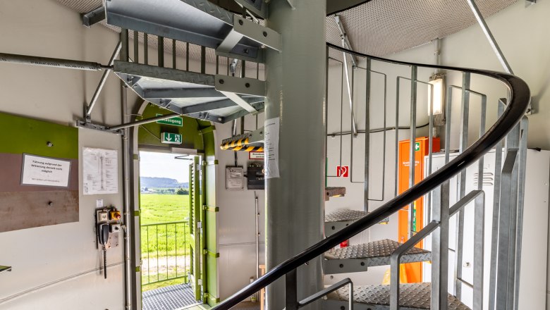 Innenansicht eines Windrads mit Wendeltreppe und geöffneter Tür nach draußen.